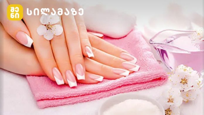 Hands with a pink French manicure resting on a folded pink towel at a spa