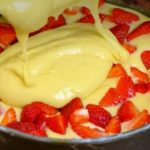 Cake batter is poured into a round baking pan surrounded by fresh strawberry slices, ready to bake.