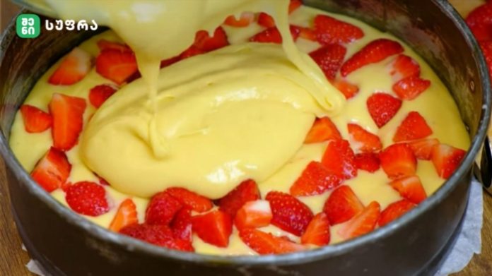 Cake batter is poured into a round baking pan surrounded by fresh strawberry slices, ready to bake.