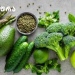 Assortment of fresh green vegetables and a green apple on a gray surface.