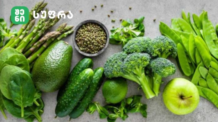 Assortment of fresh green vegetables and a green apple on a gray surface.