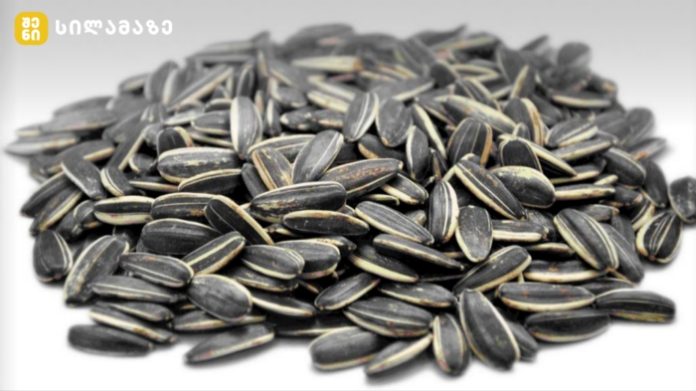 Pile of black striped sunflower seeds on a white surface, arranged in a mound.