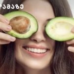 Young woman holding avocado halves over her eyes and smiling playfully.