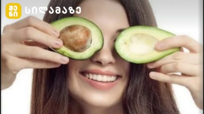 Young woman holding avocado halves over her eyes and smiling playfully.