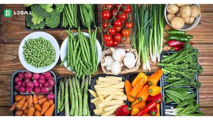 Wide assortment of fresh vegetables laid out on a wooden table, including broccoli, tomatoes, peppers, beans, carrots, and potatoes.