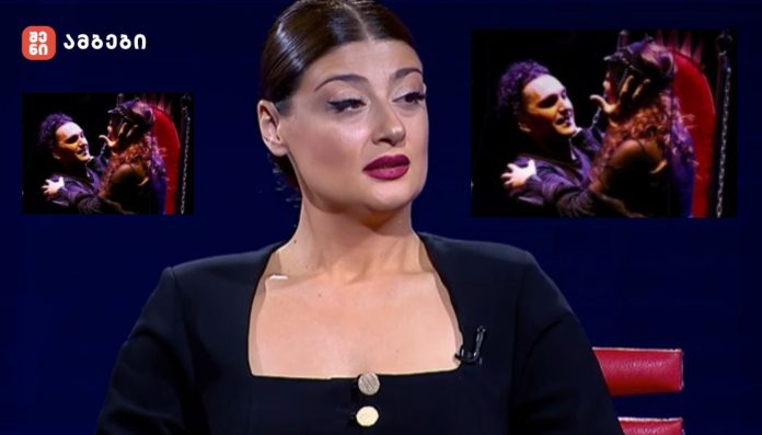 TV host on a dark blue studio set with two inset images of a couple embracing on a stage in opposite corners, logo in the top-left corner.