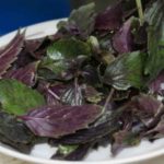 Bowl of fresh purple basil leaves on a white plate, showing green and deep purple foliage.