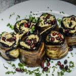 Plate of eggplant rolls filled with a light filling, topped with pomegranate seeds and chopped herbs.