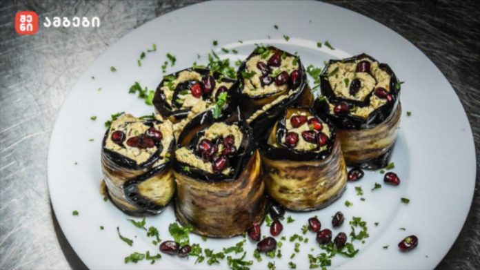 Plate of eggplant rolls filled with a light filling, topped with pomegranate seeds and chopped herbs.