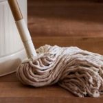 Cotton mop head resting on a wooden floor beside a white bucket, ready for cleaning transport scene.