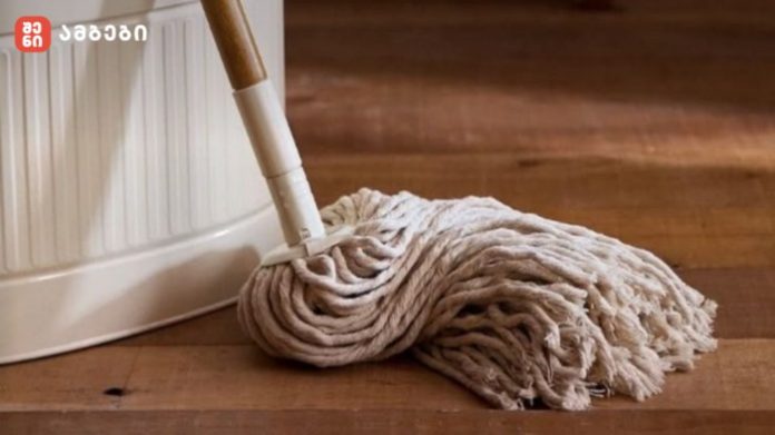 Cotton mop head resting on a wooden floor beside a white bucket, ready for cleaning transport scene.