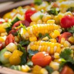 Colorful corn salad with cherry tomatoes, cucumber, yellow peppers and fresh herbs in a wooden bowl.