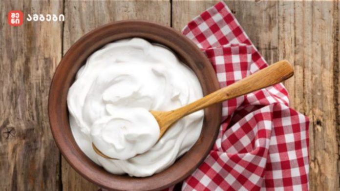 Bowl of creamy yogurt with a wooden spoon on a rustic wooden table, beside a red-and-white checkered napkin.