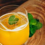 Glass of orange juice with a mint leaf garnish on a wooden board in a rustic setting