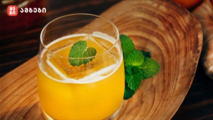 Glass of orange juice with a mint leaf garnish on a wooden board in a rustic setting