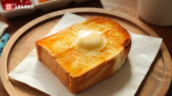A slice of toasted bread with a pat of butter on a white napkin, placed on a wooden plate, ready for breakfast.