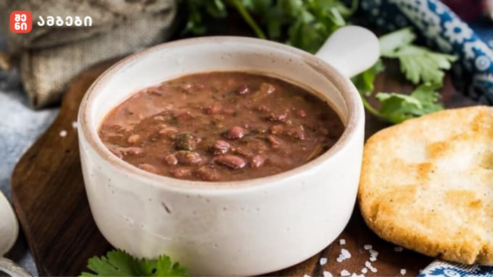 White ceramic bowl of hearty bean soup with a toasted bread slice on a wooden board, garnished with parsley.
