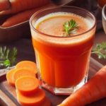 Fresh carrot juice in a glass on a wooden board, with carrot slices and a bowl of shredded carrots in the background and greens for garnish.