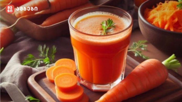 Fresh carrot juice in a glass on a wooden board, with carrot slices and a bowl of shredded carrots in the background and greens for garnish.