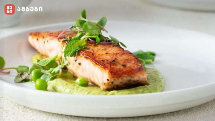 Pan-seared salmon fillet on a green pea-mint sauce with peas and microgreens on a white plate.