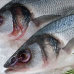 Two raw fish laid on crushed ice with a lemon slice and dill garnish, branding in the top-left corner.
