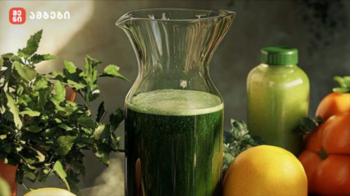 Green juice in a glass pitcher surrounded by fresh herbs and citrus on a kitchen counter