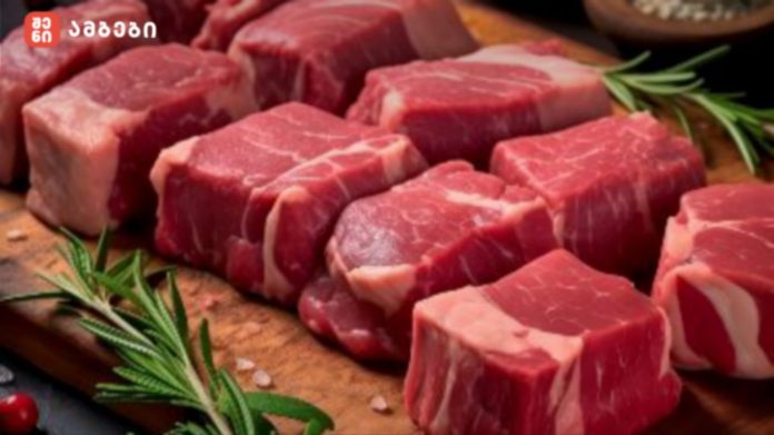Raw beef cubes with marbling on a wooden cutting board, garnished with rosemary sprigs.