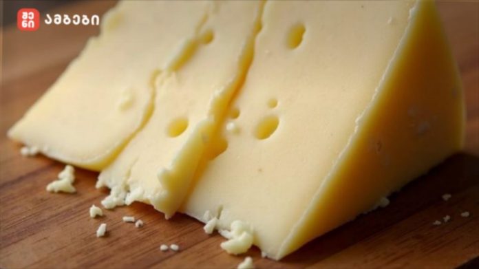 Wedge of yellow cheese sliced on a wooden board, with small cheese crumbles around it.