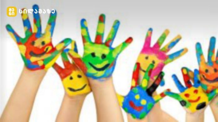 Childrens' hands painted in bright rainbow colors with smiley faces, raised together in a playful art scene.