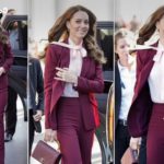 Woman in a burgundy pantsuit exits a black car, smiling, with colleagues nearby behind her.