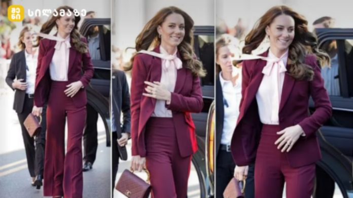 Woman in a burgundy pantsuit exits a black car, smiling, with colleagues nearby behind her.