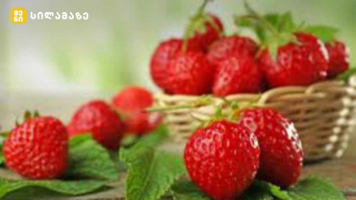 Fresh ripe strawberries in a wicker basket on a wooden surface, green garden background.