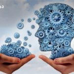 Two hands hold blue gear-filled silhouettes of a head, illustrating idea exchange or brainpower.
