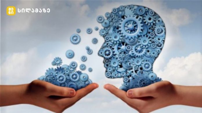 Two hands hold blue gear-filled silhouettes of a head, illustrating idea exchange or brainpower.