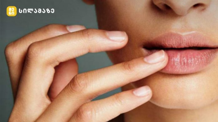 Close-up of a person’s lips with two fingers gently touching the lower lip, logo in the top-left corner