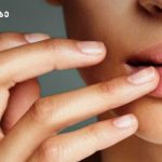 Close-up of a person touching their lips with two fingers, highlighting smooth pink lips; a logo with Georgian text appears in the top-left corner.