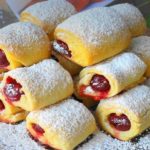 Rolls of yellow pastry filled with cherries, dusted with powdered sugar on a decorative platter