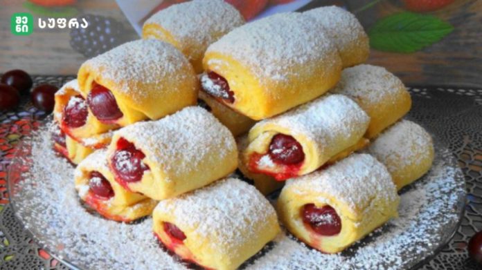 Rolls of yellow pastry filled with cherries, dusted with powdered sugar on a decorative platter