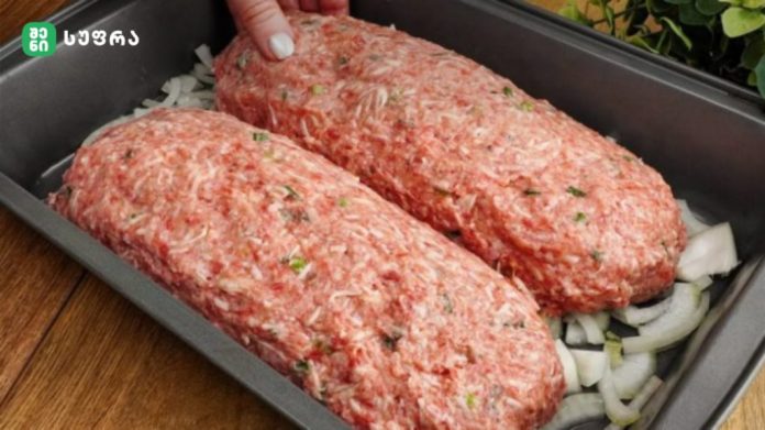 Two raw seasoned ground beef loaves in a pan over chopped onions, ready to bake, with herbs visible in the meat mixture