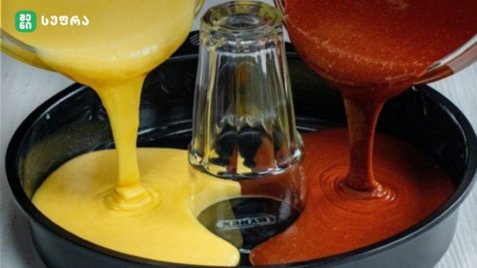 Colorful paint being poured into a round mold from left yellow and right orange-red streams meeting near a glass bottle in the center.