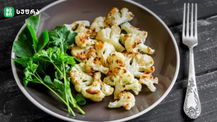 Plate of roasted cauliflower florets with a greens garnish on a dark wooden table, beside a decorative fork.