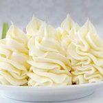 Plate of white buttercream rosettes piped in decorative swirls on a plate