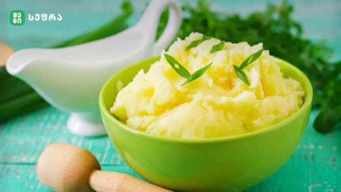 Green bowl of creamy mashed potatoes garnished with chives on a turquoise wooden table.