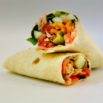 Two fresh wraps filled with cucumber, tomatoes, peppers, greens and pink shredded protein, stacked on a white surface; red logo watermark in the upper-left corner.