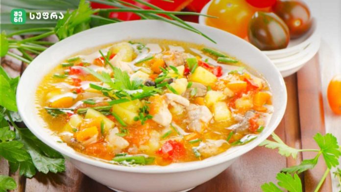 Bowl of hearty vegetable soup with potatoes, carrots, and herbs on a wooden table, garnished with parsley.