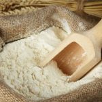 Burlap sack of flour with a wooden scoop resting inside the flour.
