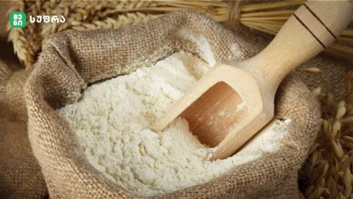 Burlap sack of flour with a wooden scoop resting inside the flour.