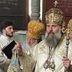 Orthodox bishops in ornate white and gold vestments during a ceremony, central figure holding a ceremonial staff.