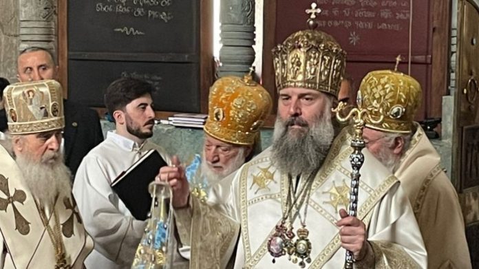 Orthodox bishops in ornate white and gold vestments during a ceremony, central figure holding a ceremonial staff.