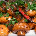 Shiny glazed roasted baby potatoes garnished with chopped parsley and a red chili pepper in a brown sauce.